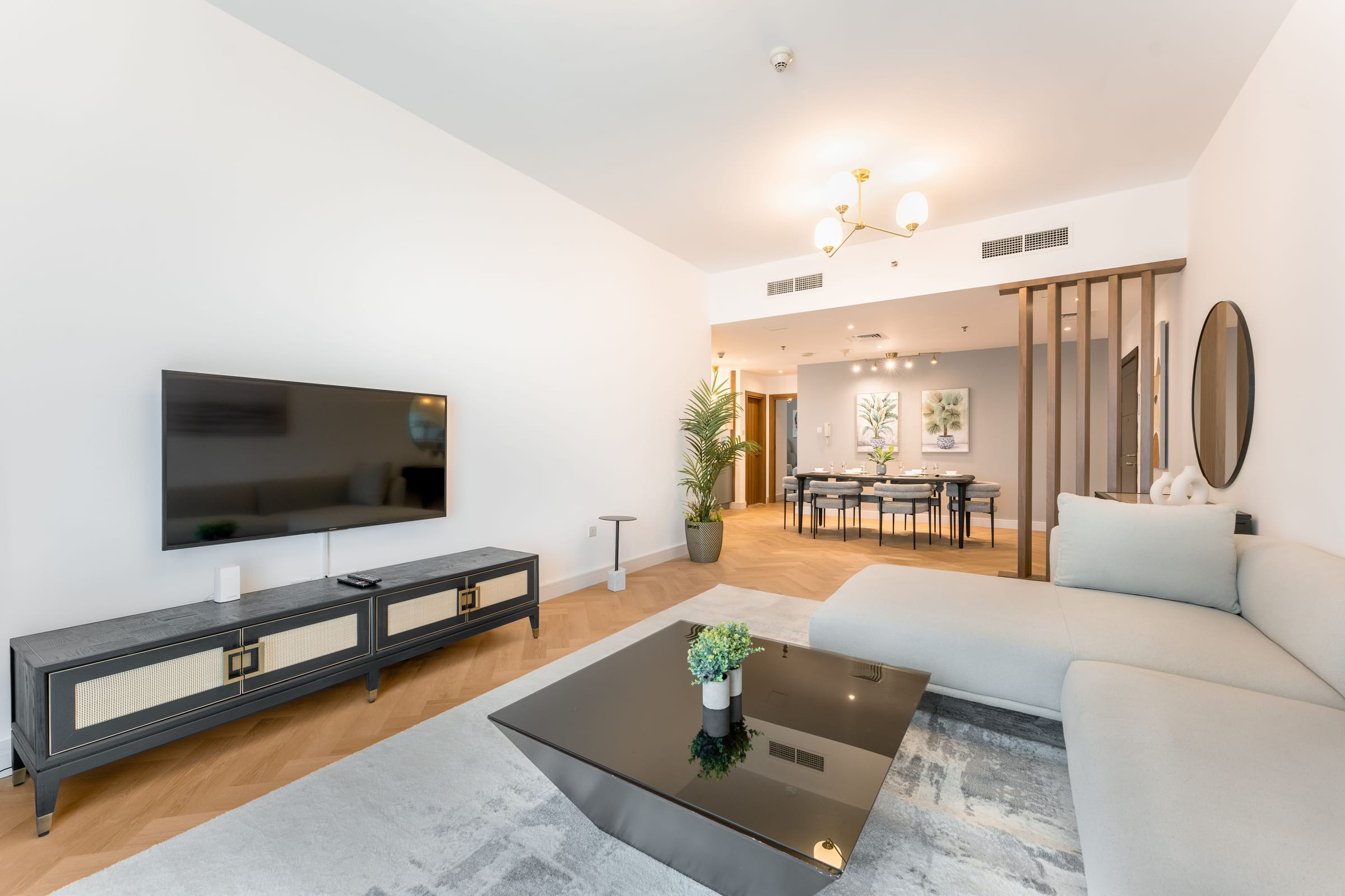 Séjour contemporain avec canapé d’angle beige, meuble TV et salle à manger en enfilade derrière une claustra en bois