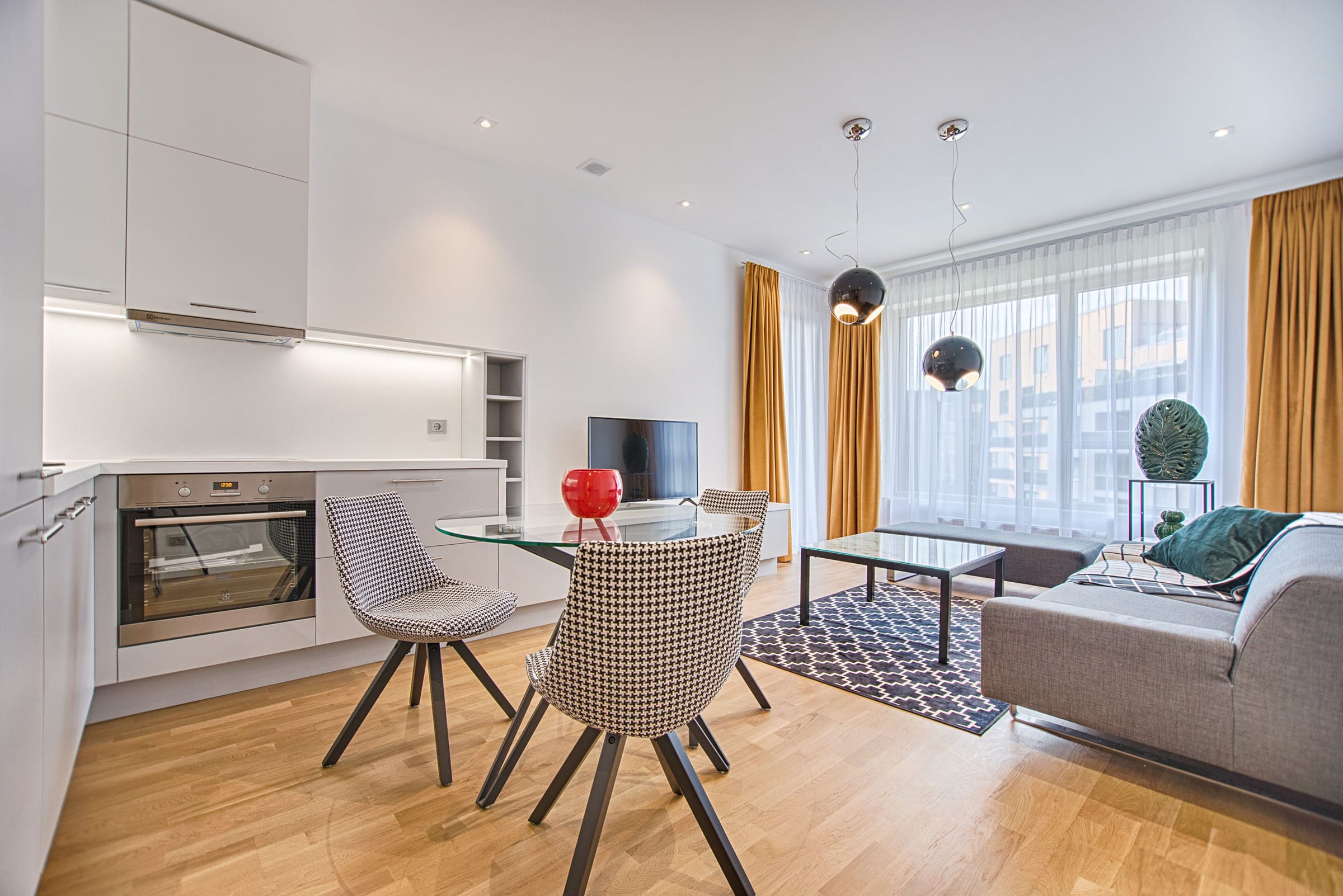 Séjour avec cuisine ouverte équipée, coin repas et rideaux moutarde dans un appartement lumineux