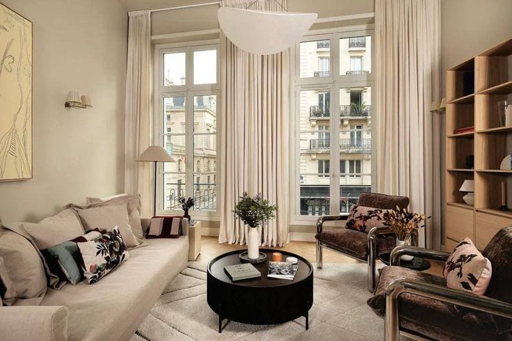 Séjour parisien sous haute hauteur, rideaux toute hauteur et fenêtres sur immeubles haussmanniens