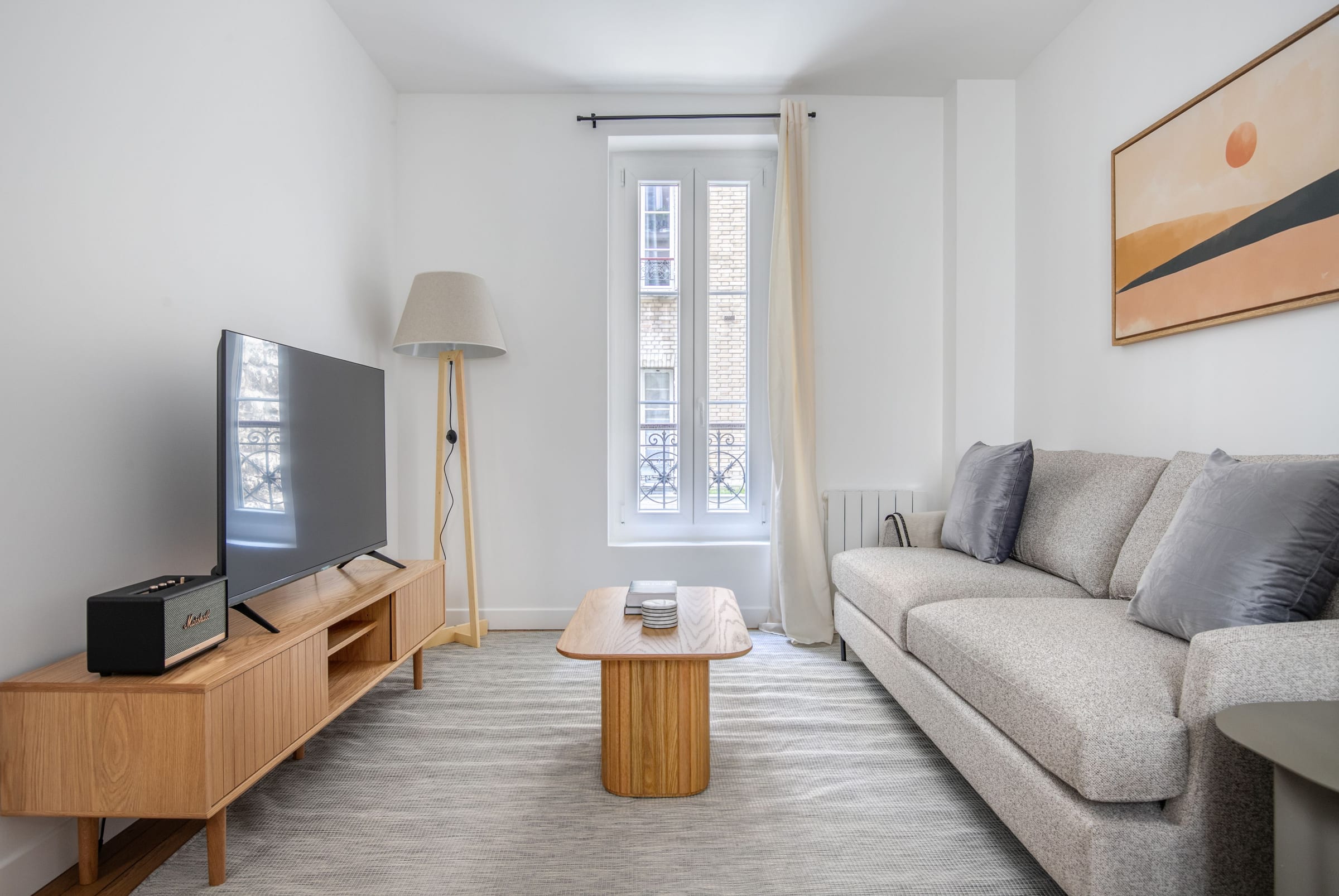 Séjour parisien avec fenêtre sur rue, canapé d’angle clair et meuble TV en bois